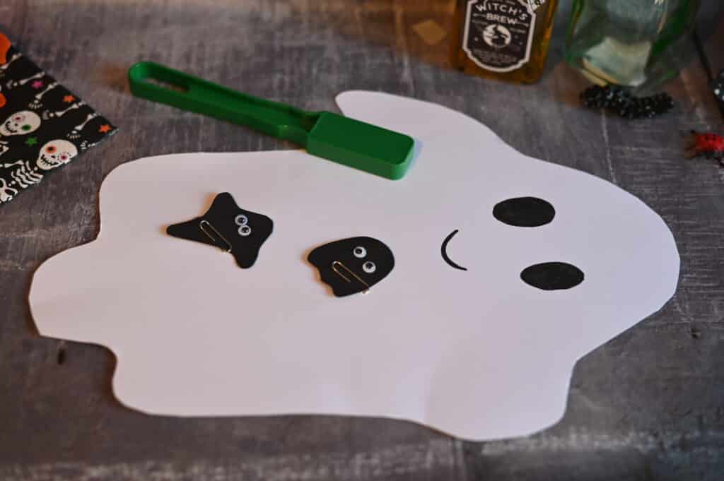 a large ghost made from white card with two smaller black card ghosts on top with googly eyes and a paperclip