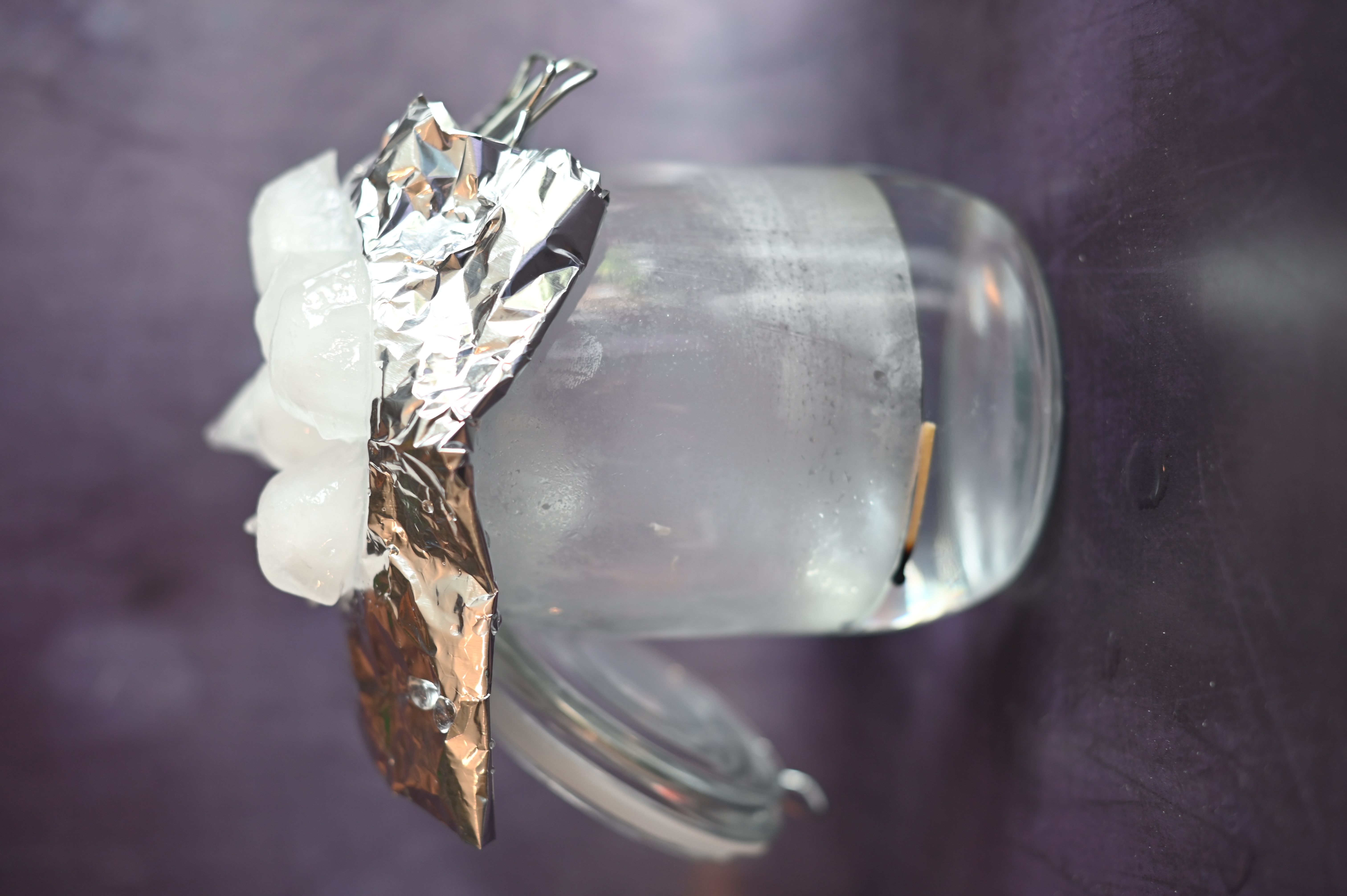 A glass jar, one quarter full of warm water with foil and ice on top