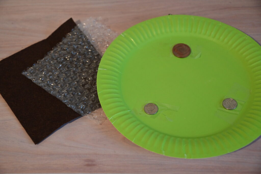 paper plate with three coins attached, felt and bubble wrap for a curling STEM Challenge